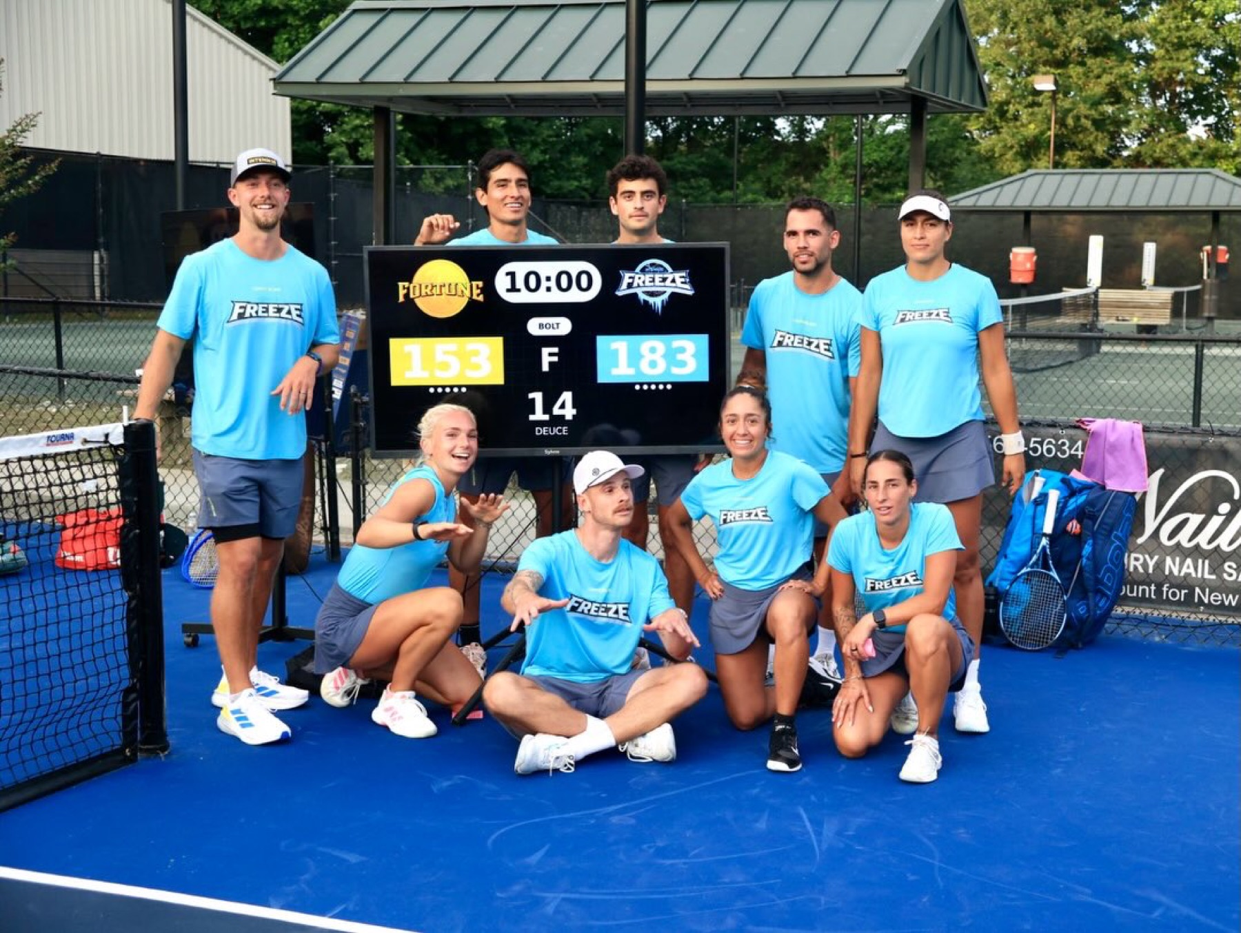 Players posed around a portable scoreboard on an outdoor hard court.