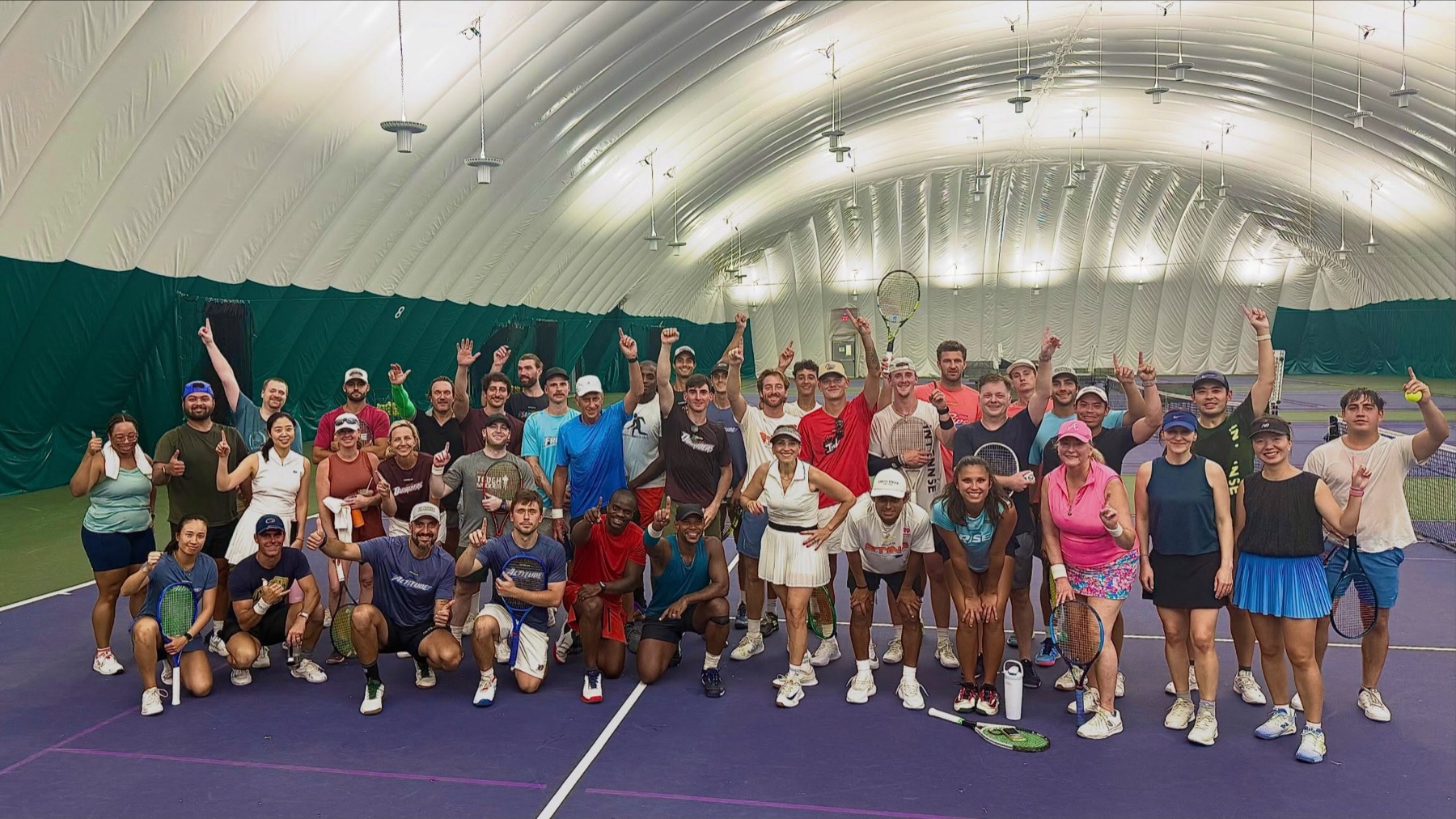 About fifty players of mixed ages on club hard courts inside an inflatable dome.