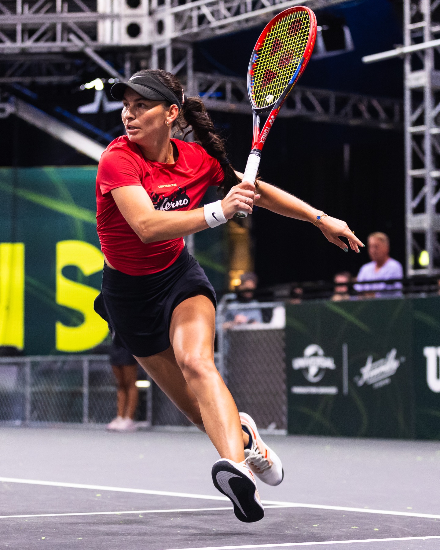 A player reaching wide for a forehand under arena lights.